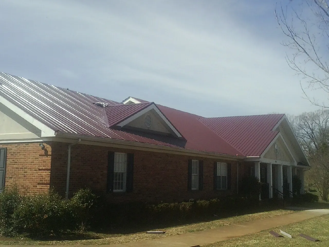 Red metal roof with gabled entries on a long brick building, from a Hail Damage Roof Repair job in Marshall