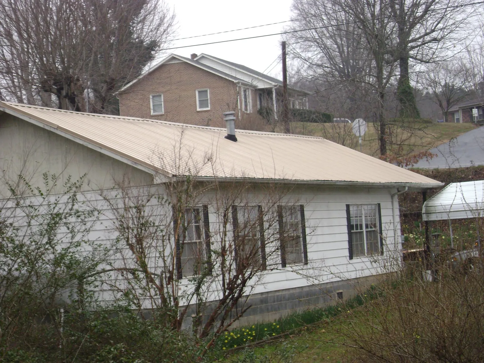 Tan metal roof on a white sided house set into a hillside — Commercial Roofing by Roofing Brothers in Marshall